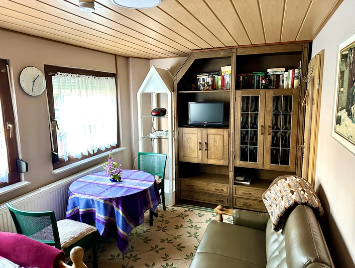 FeWo Mira 1 Herford-Stanojevic (6).jpg Wohnzimmer mit gemütlicher Sitzecke, Holzmöbeln, TV und dekorativem Tisch in einer Ferienwohnung.