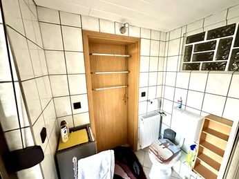 Badezimmer mit Toilette, Waschbecken, Badewanne und wandmontierten Regalen, hell gefliest.