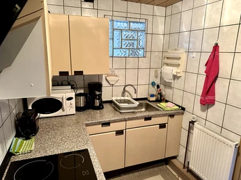 FeWo Mira 1 Herford-Stanojevic (2).jpg Moderne Küche mit Herd, Spüle und Kaffeemaschine. Fliesenwände und ein kleines Fenster vorhanden.