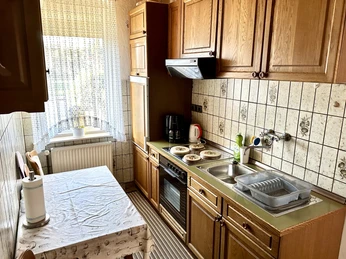 FeWo Mira Herford-Stanojevic (2).jpg Holzküche mit Küchentisch, Stühlen, Elektroherd, Spüle und Kaffeetasse auf der Arbeitsplatte. Fenster links.