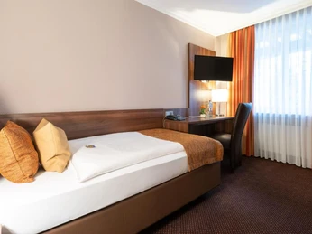 Business Einzelzimmer im Hotel im Park, Haan Einzelzimmer mit Schreibtisch, Flachbildfernseher und Bett, modern eingerichtet und gut beleuchtet.