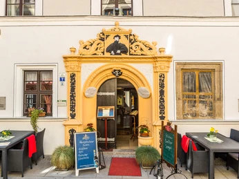 Romantik Hotel Deutsches Haus Eingangsportal Eingang eines historischen Gebäudes mit gelbem Torbogen, dekorativen Elementen und Schildern, umgeben von Tischen mit roten Decken und Blumen.