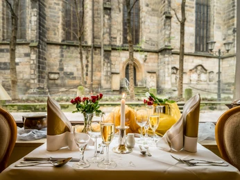 Restaurant in the Romantik Hotel Deutsches Haus Elegant gedeckter Tisch mit brennender Kerze, Sektgläsern und roten Rosen vor einem großen Fenster mit Blick auf eine alte Steinmauer.