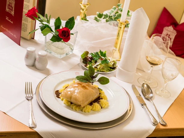 Cabbage roulade in the restaurant of the Romantik Hotel Deutsches Haus Pirna Elegantly laid table with a plate of stuffed cabbage on mashed potatoes, salad, red wine glass, candles and a red rose in a vase.