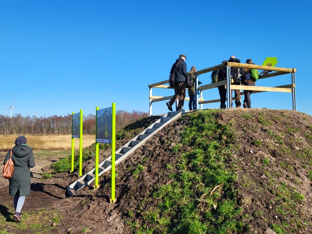 Theikenmeer-Runde, Werlte - Hümmling-Pfade, Beobachtungshügel Moorwiesen ©Naturpark Hümmling (3).jpg Mehrere Personen auf einem hölzernen Aussichtshügel mit Blick über Moorwiesen und Windräder.