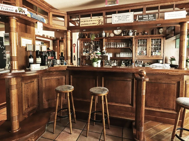 AltePost.Poststube.jpg Gemütliche, rustikale Bar mit Holzmöbeln und Barhockern, dekoriert mit Pflanzen und Flaschen.