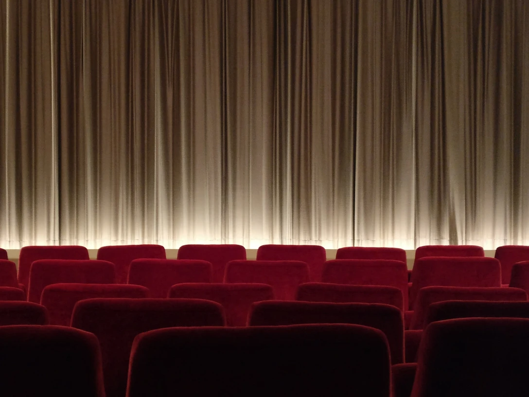Mobiles Kino Niedersachsen Rote Kinositze in Reihen vor geschlossenem, beleuchtetem Vorhang in einem Kinosaal.