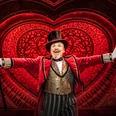 Moulin Rouge! The musical Ein strahlender Schauspieler im eleganten, roten Frack, mit Zylinder und Stock, vor leuchtendem Herzmotiv.A radiant actor in an elegant red tailcoat, with top hat and cane, in front of a glowing heart motif.