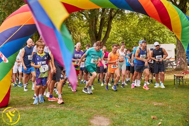 SC Janus Queer Games Läuferinnen und Läufer starten unter einem bunten Regenbogenbogen in einem Parklauf.