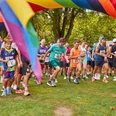 SC Janus Queer Games Läuferinnen und Läufer starten unter einem bunten Regenbogenbogen in einem Parklauf.