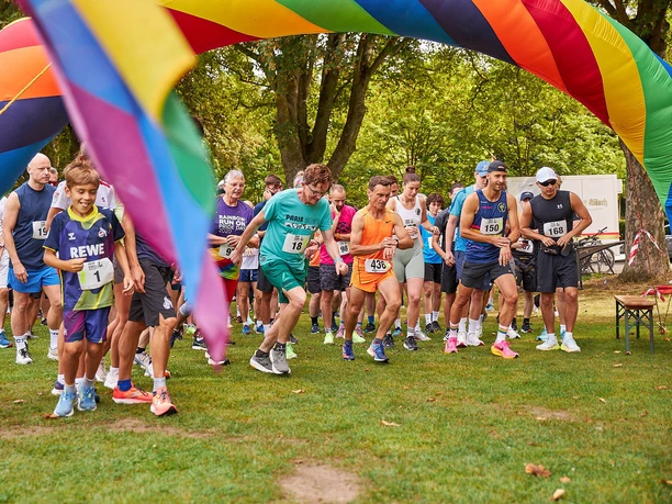 SC Janus Queer Games Runners start under a colorful rainbow arch in a park run.