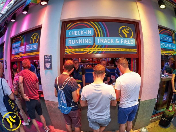 SC Janus Queer Games Anmeldung Teilnehmende stehen an bunt beleuchteten Check-in-Schaltern der Queer Games in Köln an.