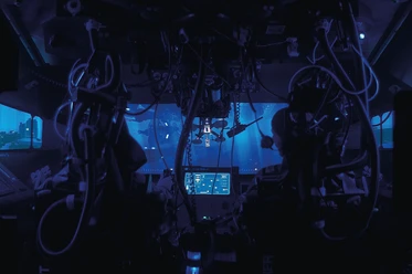 NEMO3 Blick in das Cockpit eines U-Boots mit zahlreichen Kabeln und Bildschirmen, die in blauem Licht leuchten, und einem Fenster mit Unterwasseransicht.