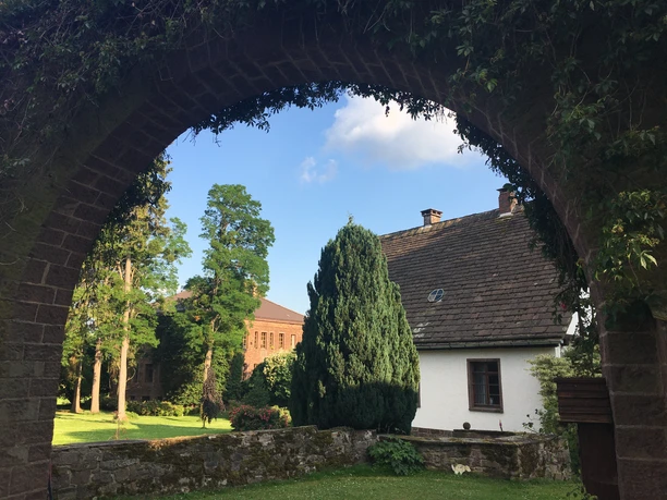 Blick durch einen Steinbogen auf Häuser der Gutshofanlage Maygadessen