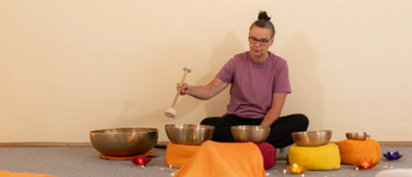 Klang- / Entspannungsreise Frau spielt Klangschalen neben liegender Person, sanftes Licht und warme Farben schaffen Ruhe.