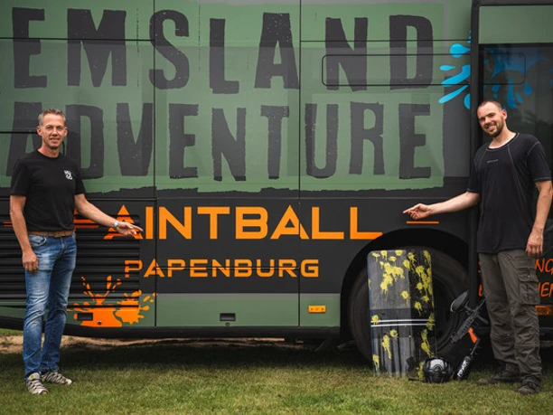 549390_8a48f83bd90d441e92e16c9af6539991~mv2.jpg Zwei Männer stehen vor einem dunkelgrünen Bus mit der Aufschrift Emsland Adventure Paintball Papenburg.