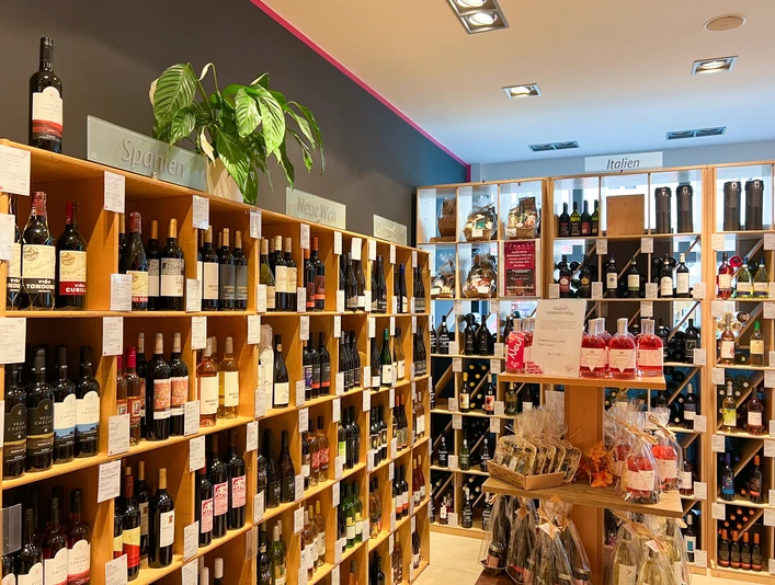 In einem Geschäft sind hohe Regale an den Wänden, die mit vielen verschiedenen Weinflaschen gefüllt sind.