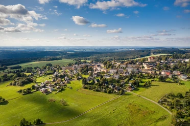 Schöneck_Sommer Luftaufnahme von Schöneck im Sommer, umgeben von grünen Wiesen und Wäldern unter blauem Himmel.