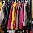 Verschiedene bunte Lederjacken hängen eng nebeneinander auf Kleiderbügeln bei einem Flohmarkt.