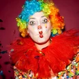 Karneval Clown Ein Clown mit bunter Perücke, rotem Kragen und Luftschlangen auf dunkelrotem Hintergrund.