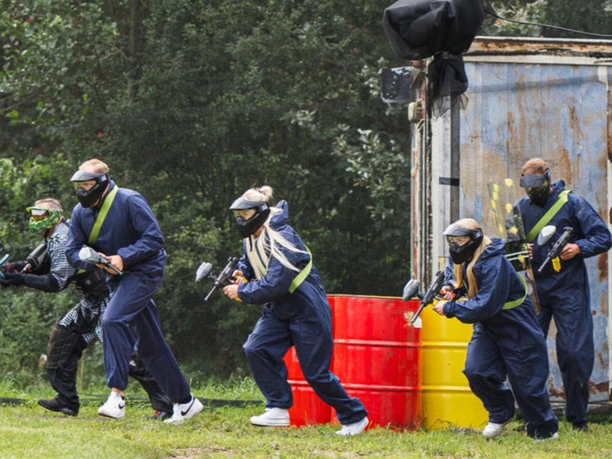 IMG_5488.jpeg Gruppe von Paintballspielern in Schutzanzügen und Masken rennt mit Markierern über ein Spielfeld.