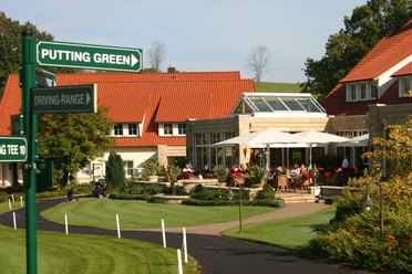Ein Golfclub mit gepflegten Grünflächen, Sonnenschirmen und Hinweisschildern zur Driving-Range.