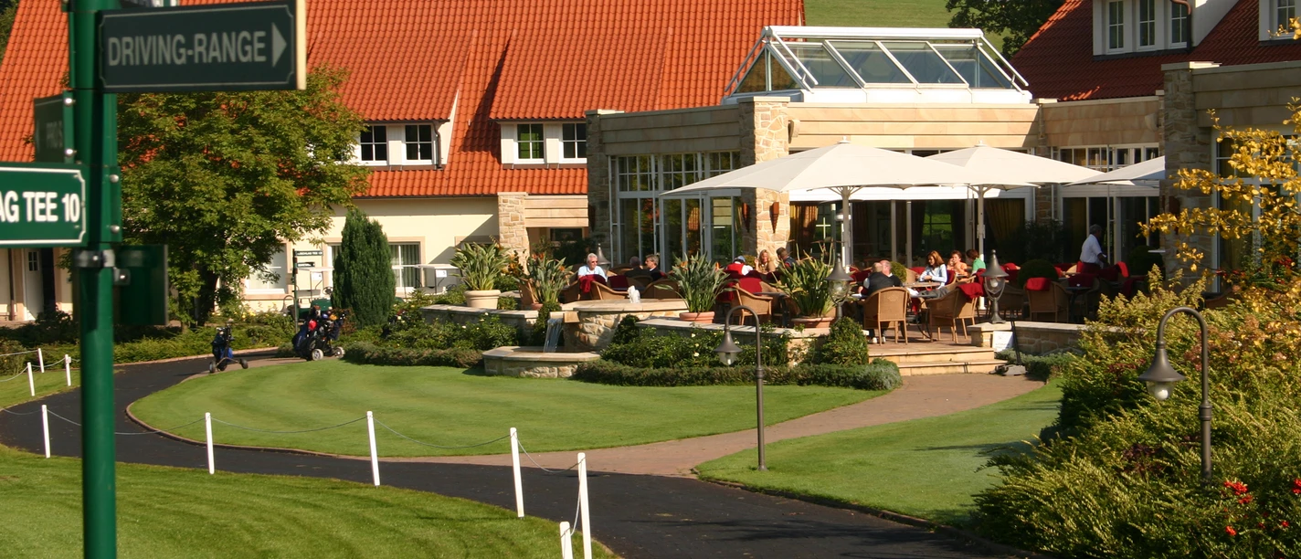 Ein Golfclub mit gepflegten Grünflächen, Sonnenschirmen und Hinweisschildern zur Driving-Range.