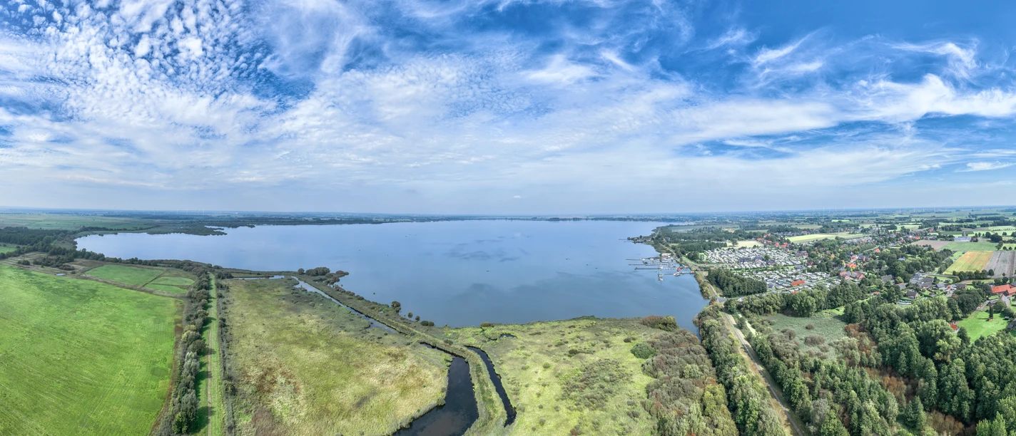 Dümmer-See Extensive lake landscape with surrounding meadows and forests under a blue sky.