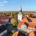 Bad Essen Kirchturm mit grünem Dach überragt Fachwerkhäuser in herbstlicher Dorfansicht.Church tower with green roof towers above half-timbered houses in an autumnal village view.Kirketårn med grønt tag tårner sig op over bindingsværkshuse i en efterårsagtig landsbyudsigt.Kerktoren met groen dak torent uit boven vakwerkhuizen in herfstig dorpsgezicht.
