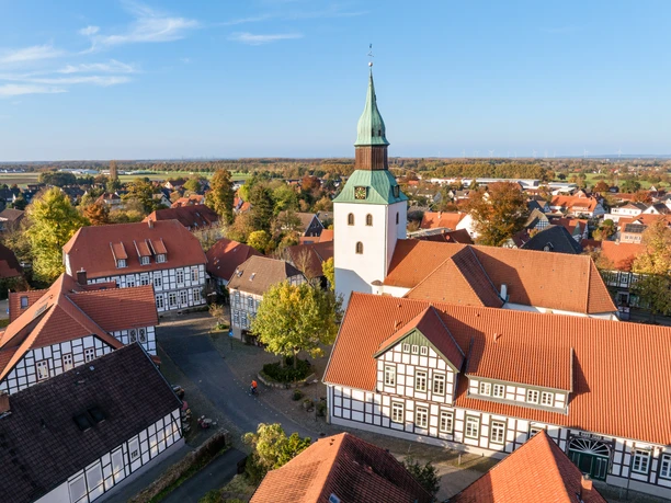 Bad Essen Kirchturm mit grünem Dach überragt Fachwerkhäuser in herbstlicher Dorfansicht.