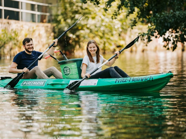 Dwie osoby siedzą w zielonym kajaku z portu miejskiego w Lipsku na kanale w Lipsku i mogą jednocześnie zbierać śmieci, Water City Leipzig, Zrównoważony rozwój