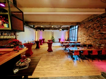 Innenraum mit großen Tischen an der rechten Wand und mehreren Stehtischen in der Mitte. Links ist eine Bartheke.