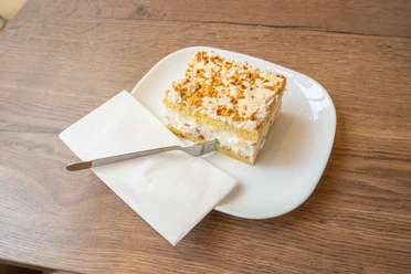Selbstgebackener Kuchen im Café Bös, Ratingen Ein Teller mit einem Stück Schichtkuchen und einer Gabel auf einer Serviette, serviert im Café.