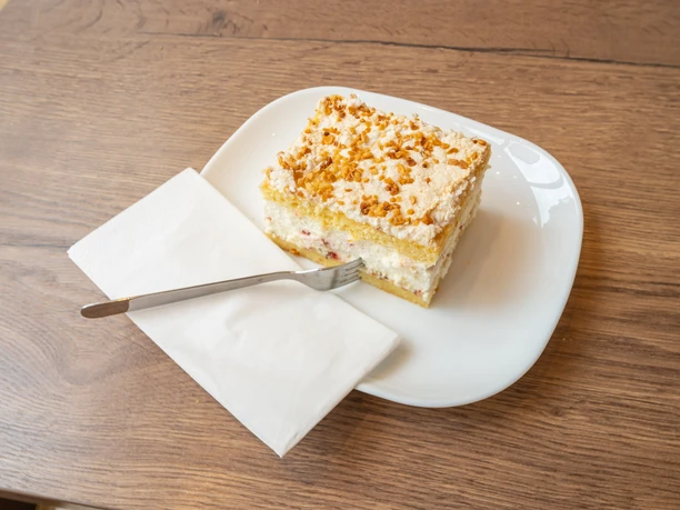 Selbstgebackener Kuchen im Café Bös, Ratingen Ein Teller mit einem Stück Schichtkuchen und einer Gabel auf einer Serviette, serviert im Café.