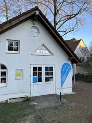 Ideentreff Bochum-Nord Kleines weißes Haus mit markantem Dreiecksgiebel und blauer Fahne vor der Eingangstür.