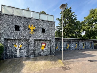 Spraygrammtechnik Bananensprayer Winckelmannstraße 11 2 Graffiti on a gray façade: banana symbols and Rolling Stones mouth illustrate the wall.