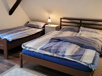 FeWo Obereickum- Doppelbett - B Schlaupitz (1).jpg Zwei Einzelbetten in einem hellen Zimmer mit Schrägdach, rustikalem Holzboden und Nachttischlampe.