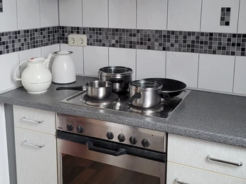 Kleine Kochnische mit zwei Kochfeldern, verschiedenen Edelstahltöpfen und Wasserkocher.