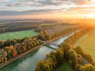 Mittellandkanal bei Bad Essen Luftaufnahme eines Kanals mit Brücke, umgeben von herbstlich gefärbten Bäumen bei Sonnenuntergang.