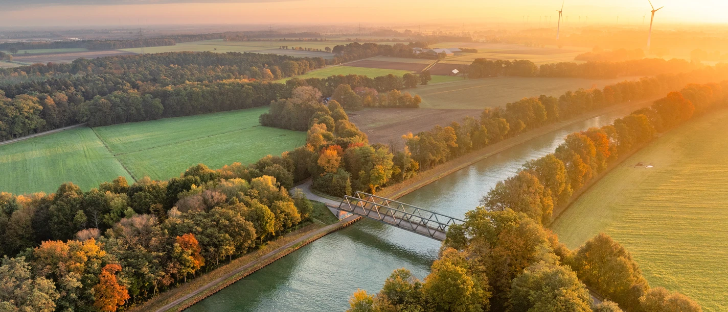 Mittellandkanal bei Bad Essen Aerial view of a canal with a bridge, surrounded by autumn-colored trees at sunset.