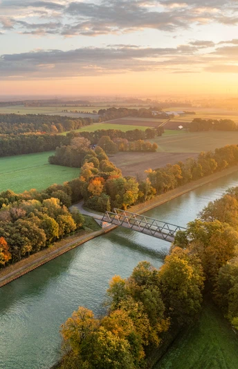 Mittellandkanal bei Bad Essen Luftaufnahme eines Kanals mit Brücke, umgeben von herbstlich gefärbten Bäumen bei Sonnenuntergang.