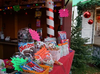 Süßes im Winter Verkaufsstand mit Süßwaren, festlicher Dekoration, Lichterkette und Weihnachtsbaum im Hintergrund.Sales stand with confectionery, festive decorations, fairy lights and Christmas tree in the background.Salgsstand med konfekture, juledekorationer, lyskæder og juletræ i baggrunden.Verkoopstand met snoepgoed, feestelijke decoraties, feeërieke verlichting en kerstboom op de achtergrond.