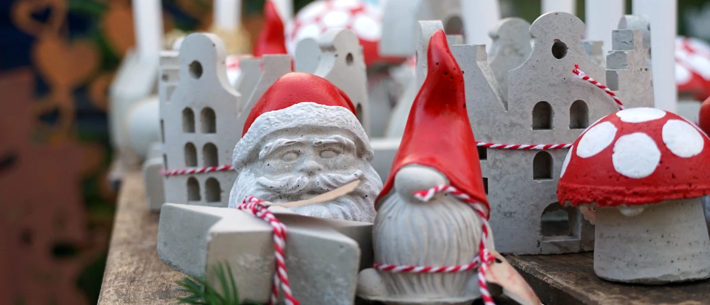Kleine Weihnachtsfiguren Weihnachtliche Figuren aus Beton mit roten Mützen und Pilzen, festlich auf einem Holztisch arrangiert.