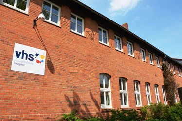 Volkshochschule_Salzgitter-Lebenstedt_HD.JPG Rote Backsteinfassade der Volkshochschule Salzgitter mit vhs-Schild und weißen Fenstern.