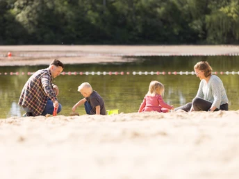 Badesee Hille Mindenerwald.Christian Schwier Juni 2023 Sommer (21).jpg Familie spielt fröhlich im Sand am Ufer eines Badesees. Wald im Hintergrund, klare Sommerstimmung.