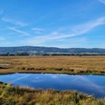 Weitläufige Moorlandschaft mit blauem Himmel und Wolken, spiegelnde Wasserflächen im Vordergrund.