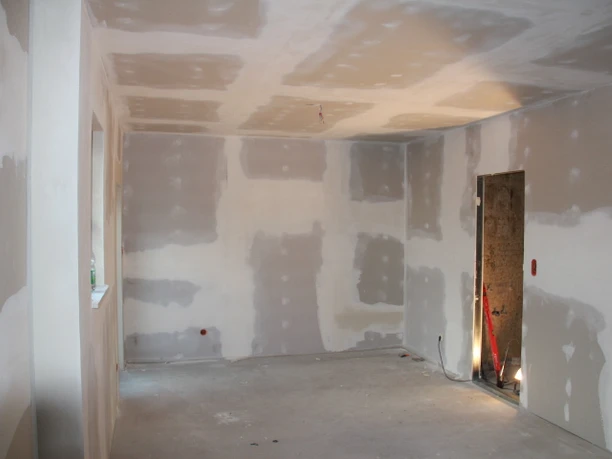 Leerer Raum im Rohbauzustand mit grauer Betonboden und freiliegenden Wänden ohne Verkleidung.