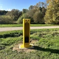 Gelbe ADAC-Fahrradreparatursäule auf Wiese, umgeben von Bäumen und einem Gehweg im Park.