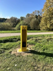 Radstation Bielefeld "Walther" Gelbe ADAC-Fahrradreparatursäule auf Wiese, umgeben von Bäumen und einem Gehweg im Park.