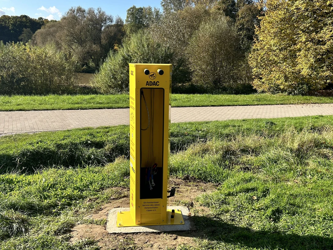 Radstation Bielefeld "Walther" Gelbe ADAC-Fahrradreparatursäule auf Wiese, umgeben von Bäumen und einem Gehweg im Park.